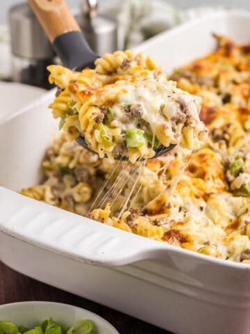 Taking a scoop of cheesesteak casserole from a baking dish.