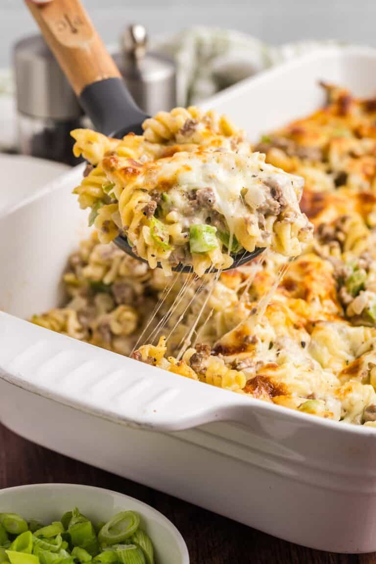 Taking a scoop of cheesesteak casserole from a baking dish.
