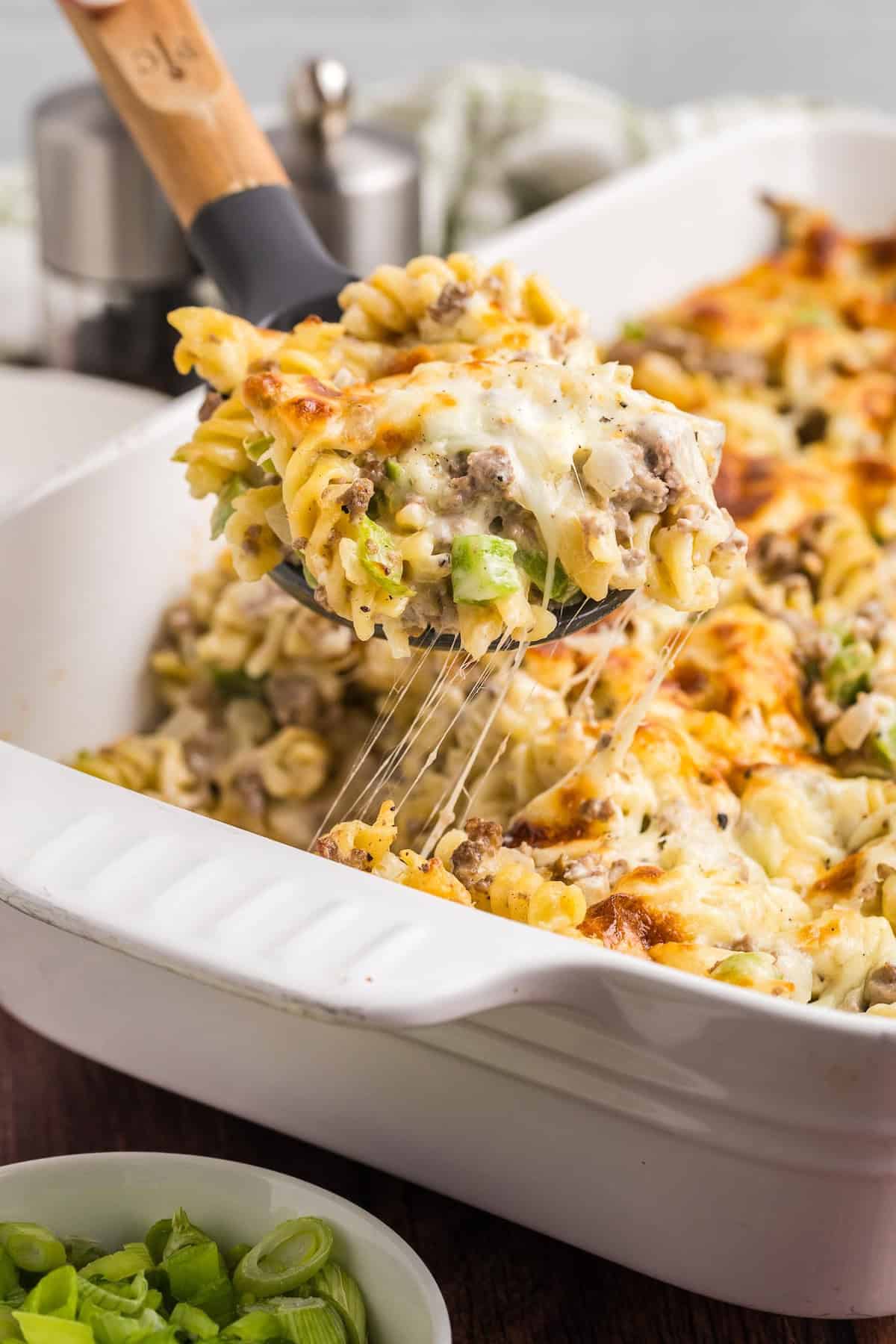 Taking a scoop of cheesesteak casserole from a baking dish.