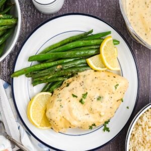 Lemon pepper chicken on a plate with green beans and lemon wedges.