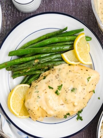 Lemon pepper chicken on a plate with green beans and lemon wedges.