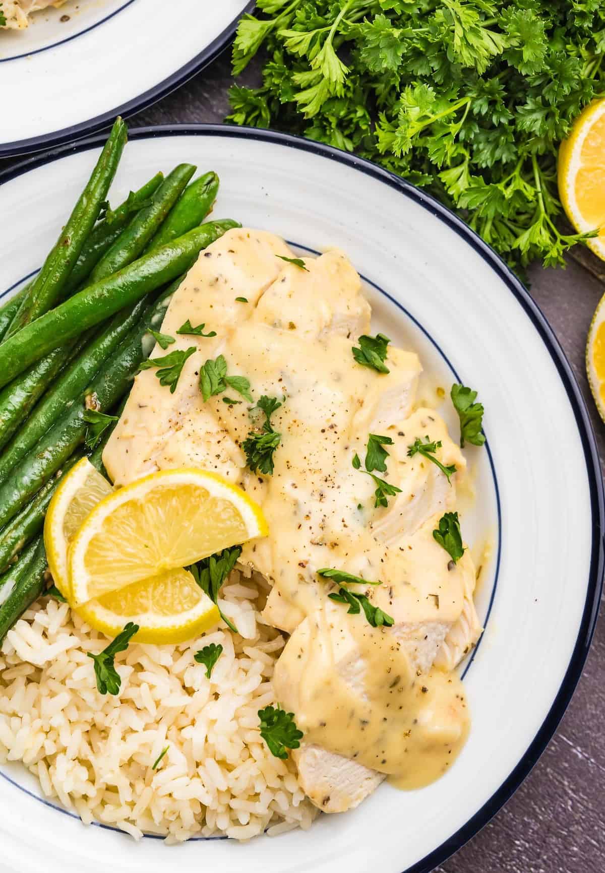 A plate of lemon pepper chicken with rice, green beans, and lemon wedges.