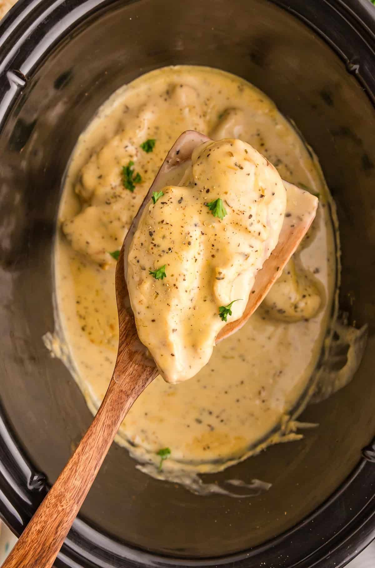 Lifting a piece of lemon pepper chicken from the slow cooker with a wooden spatula.