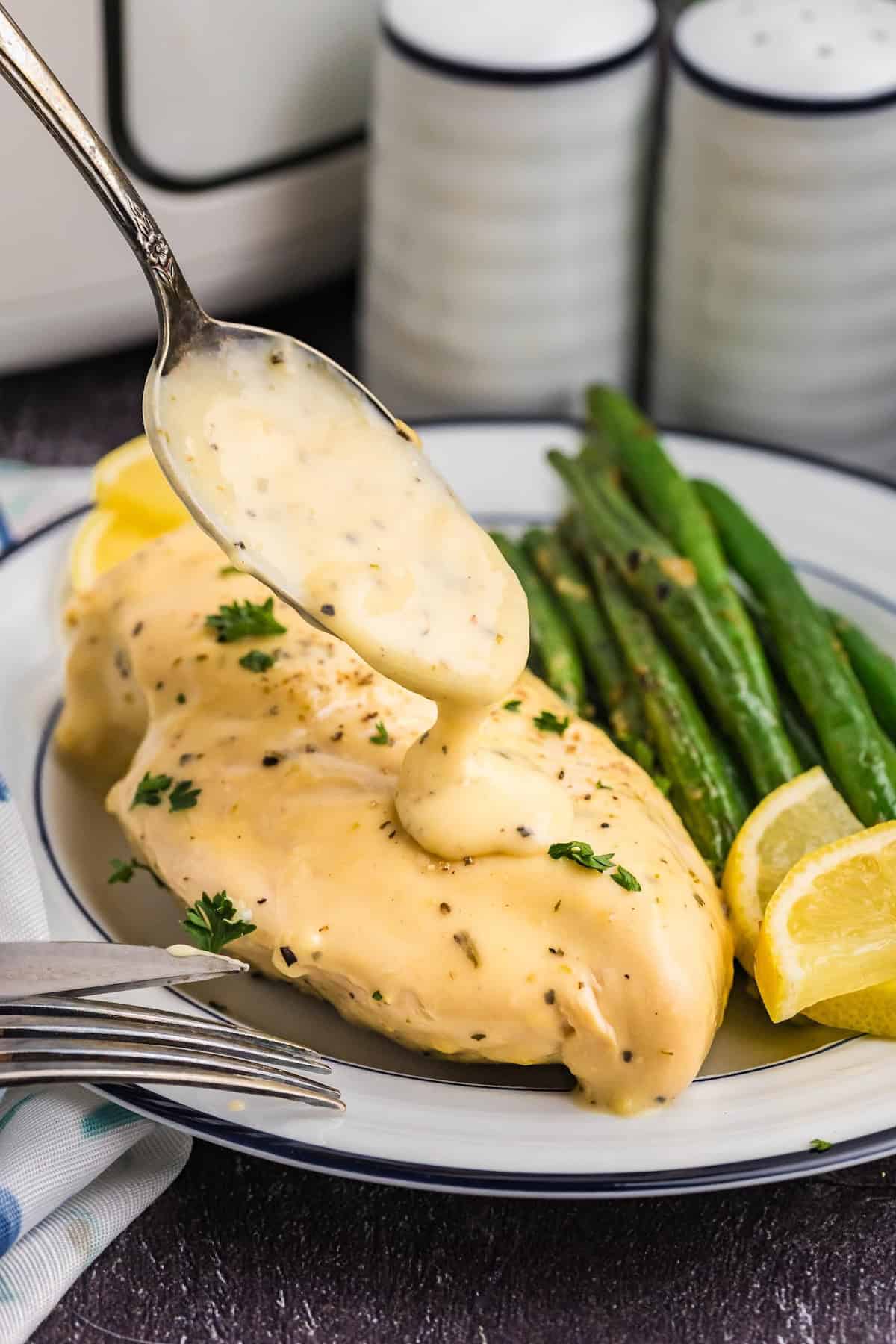 Spooning more lemon pepper sauce on slow cooker chicken on a plate.