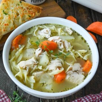 A bowl of turkey noodle soup on a table with spoons and a piece of toasted bread.