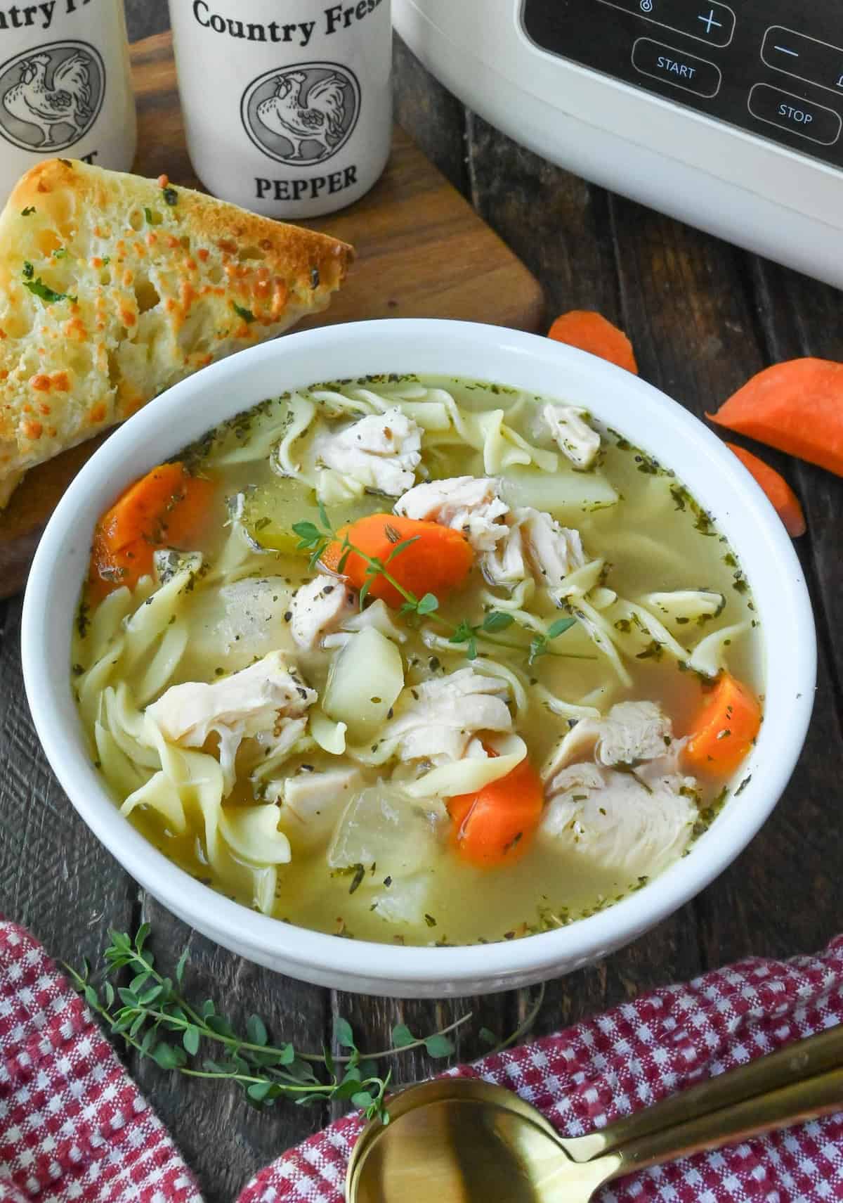 A bowl of turkey noodle soup on a table with spoons and a piece of toasted bread.