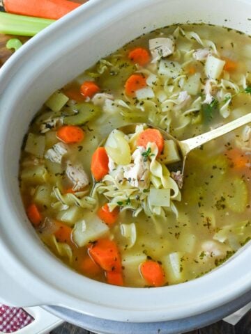 Close up of a spoon taking a scoop of slow cooker turkey soup from the crockpot.