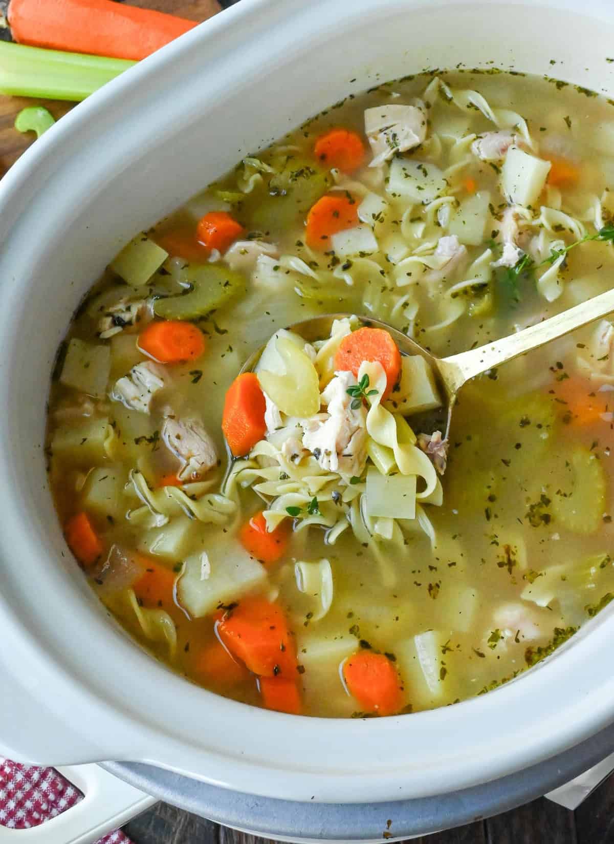 Close up of a spoon taking a scoop of slow cooker turkey soup from the crockpot.