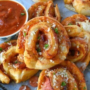 Pepperoni pinwheels on a platter with a dish of marinara sauce.