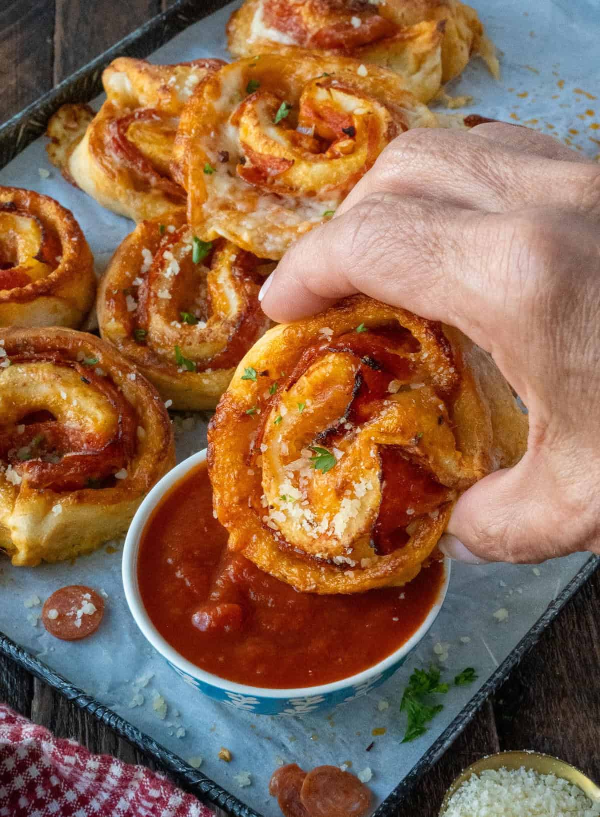 Dipping a pepperoni pinwheel in a dish of marinara sauce.