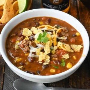 A bowl of taco chili garnished with shredded cheese and crumbled corn chips.