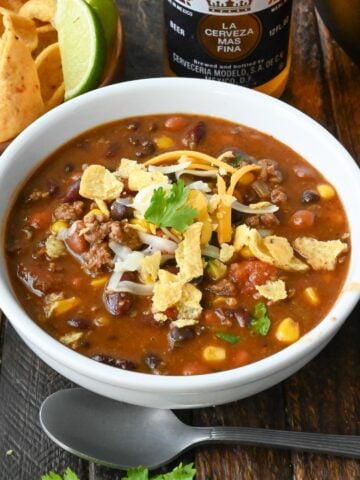 A bowl of taco chili garnished with shredded cheese and crumbled corn chips.