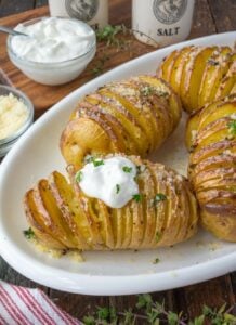Golden brown hasselback potatoes on a white serving dish with a dollop of sour cream.