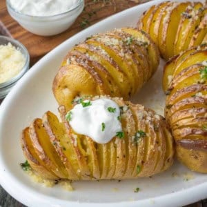 Golden brown hasselback potatoes on a white serving dish with a dollop of sour cream.