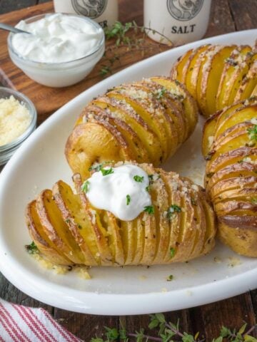 Golden brown hasselback potatoes on a white serving dish with a dollop of sour cream.