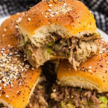 A plate of cheesesteak sliders, one of which has a bite taken out of it.