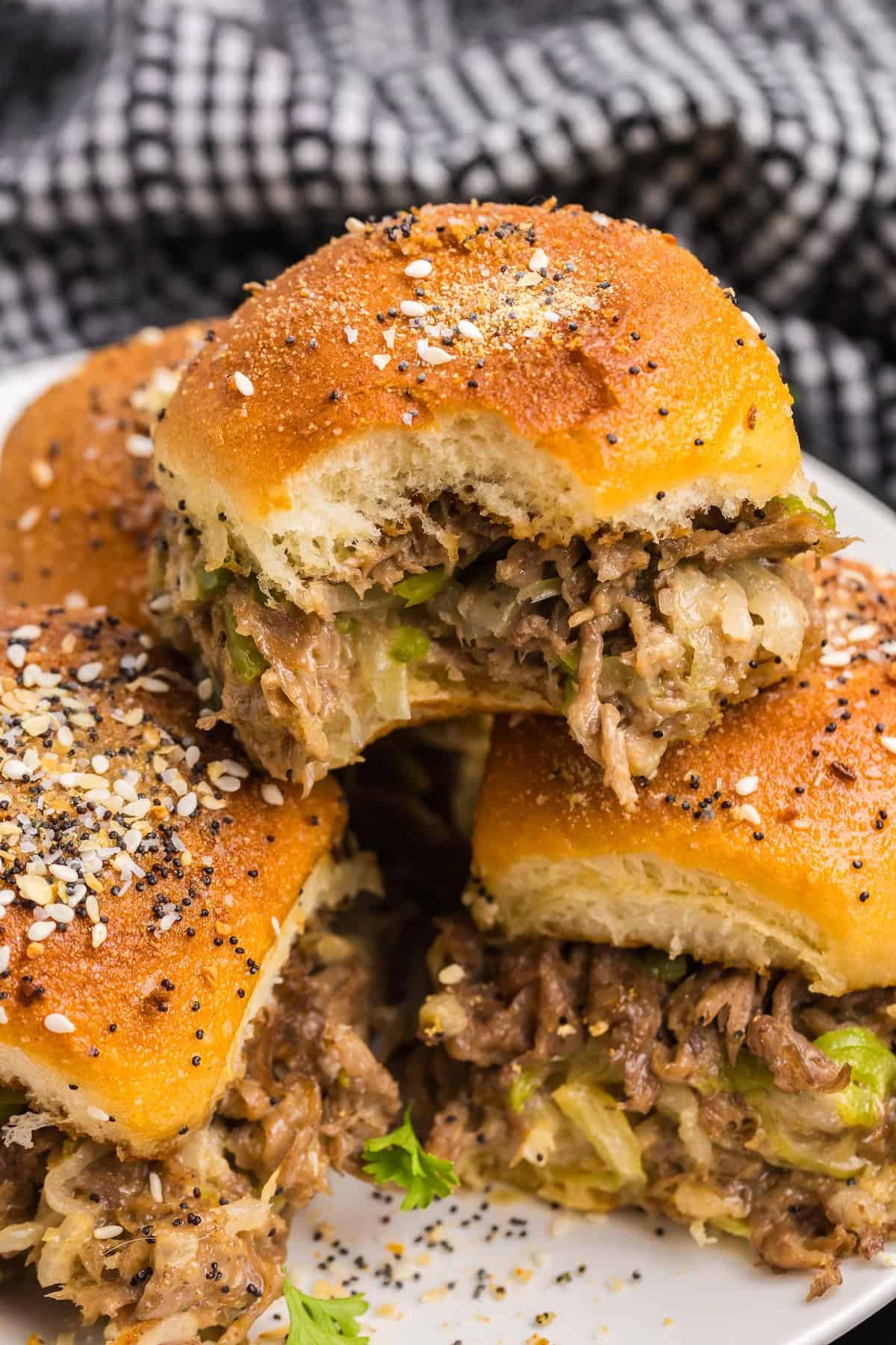 A plate of cheesesteak sliders, one of which has a bite taken out of it.