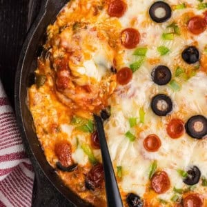 A spoon resting in a cast iron skillet of pizza dip.