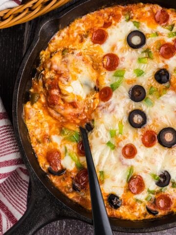 A spoon resting in a cast iron skillet of pizza dip.