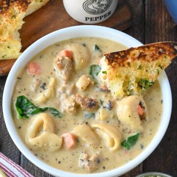 Sausage tortellini soup in a bowl with garlic bread.