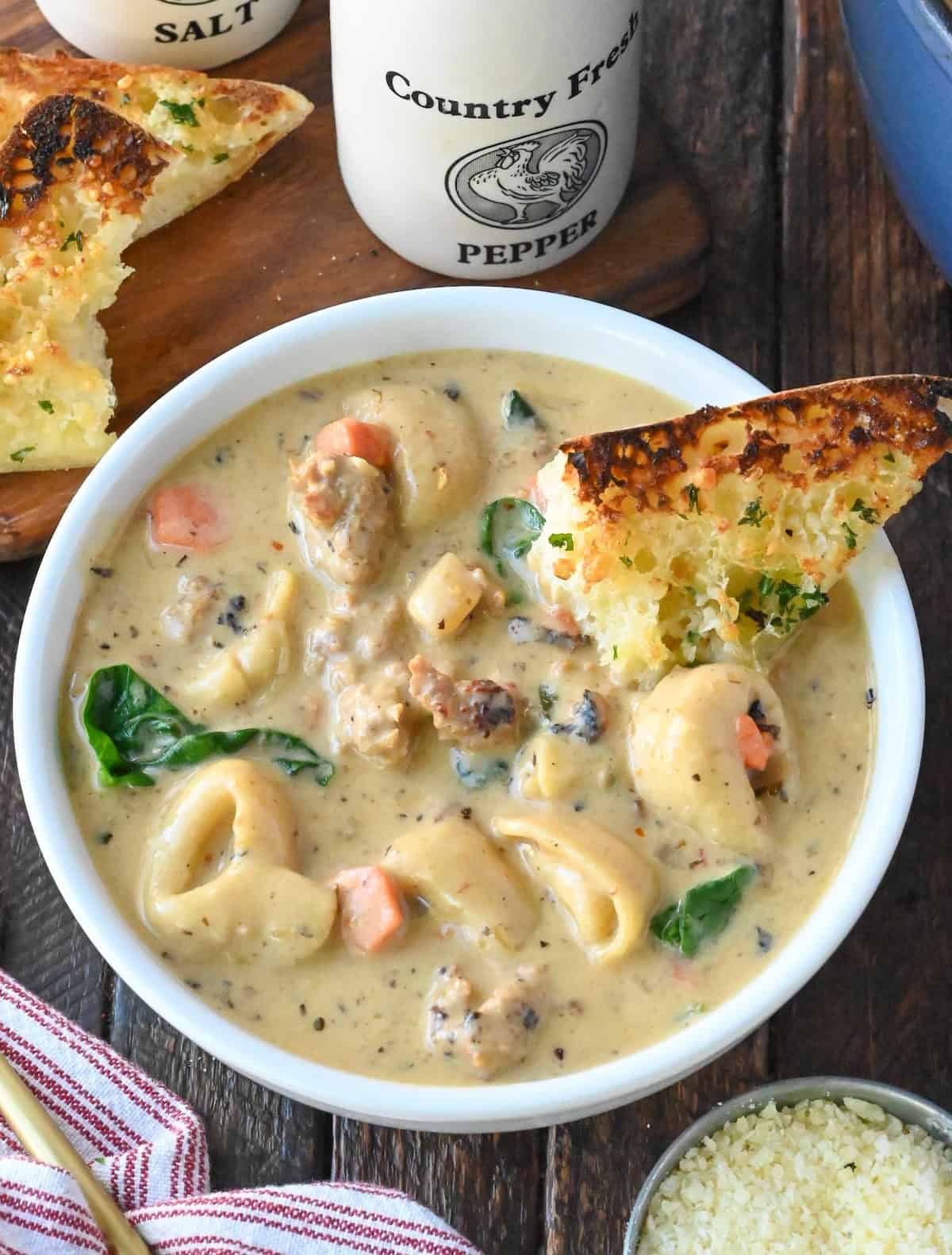 Sausage tortellini soup in a bowl with garlic bread.