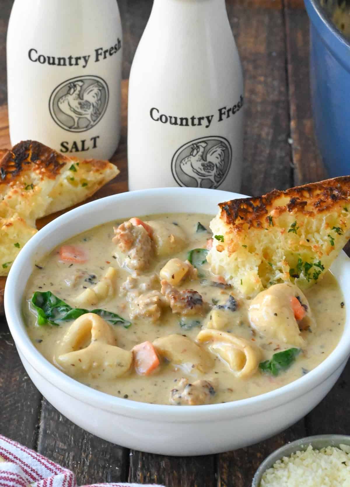 Sausage tortellini soup in a bowl with garlic bread.