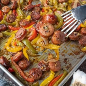 Sausage and pepper on a sheet pan with a spatula.