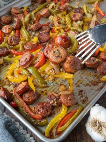 Sausage and pepper on a sheet pan with a spatula.