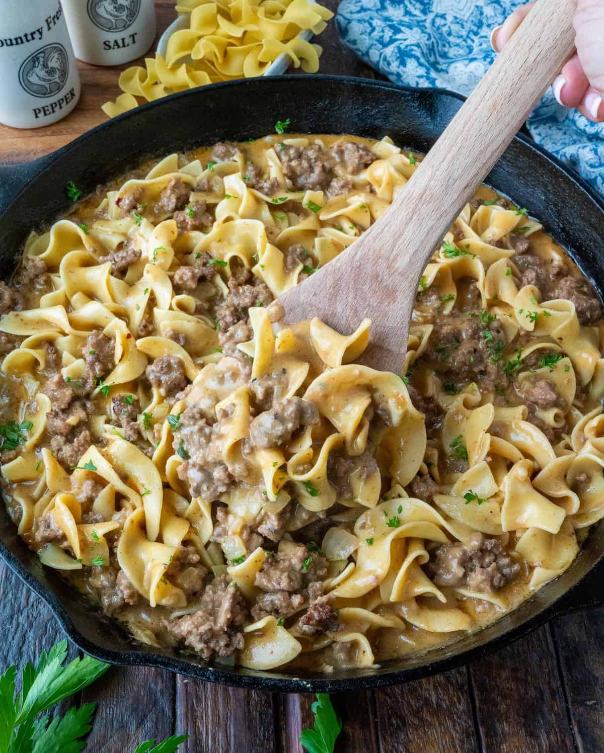 A wooden spoon scooping up some pasta from a skillet.