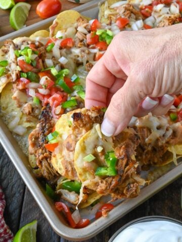 Carnitas nachos being picked up from a baking sheet.