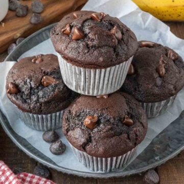 A plate of 5 chocolate banana muffins arranged in a stack.