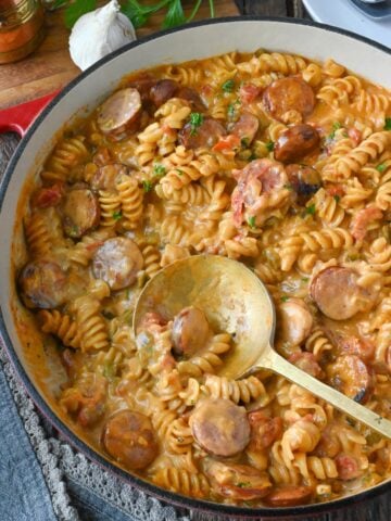 Cheesy sausage pasta skillet with a serving spoon.