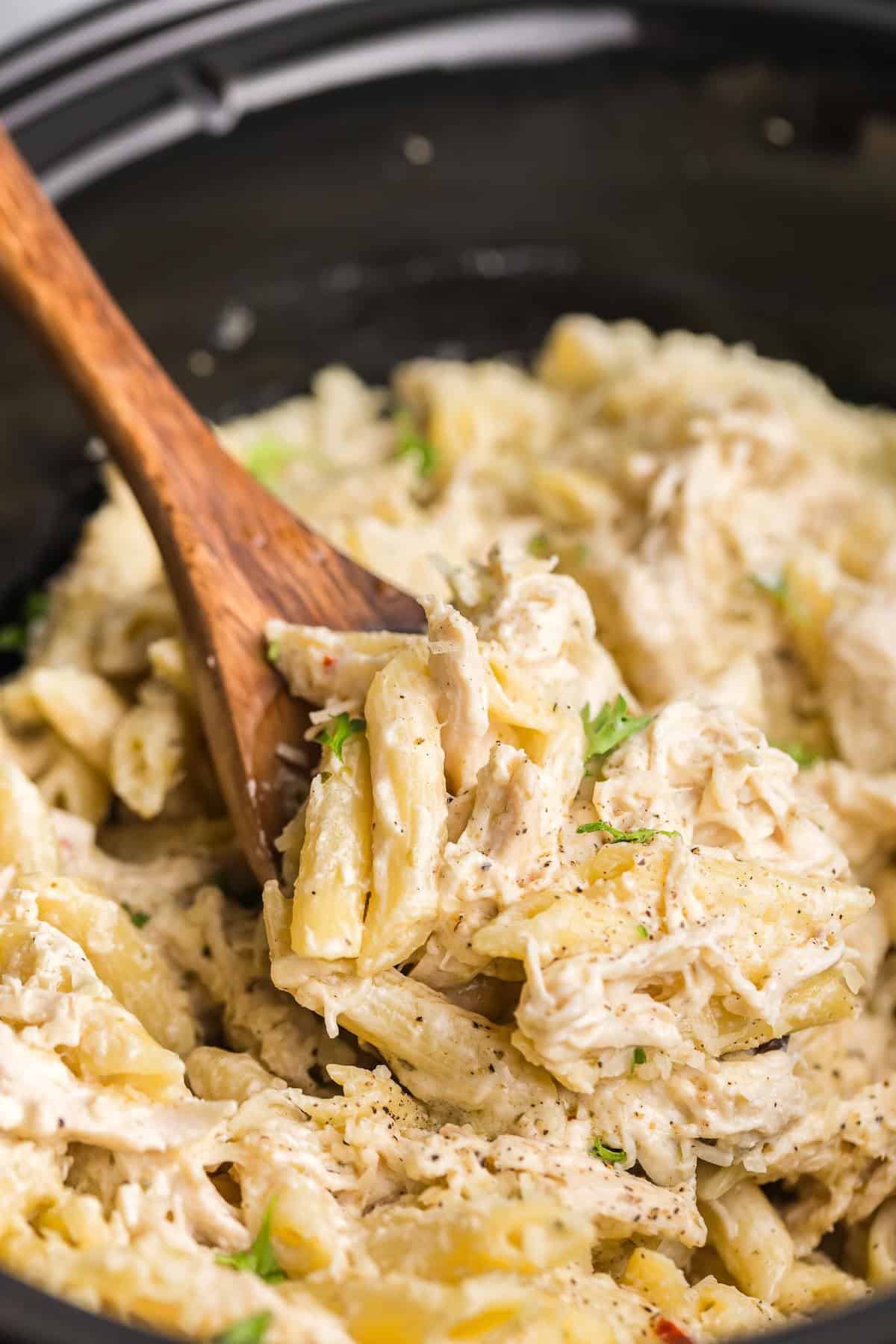 Stirring a crock pot of chicken pasta with a wooden spoon.