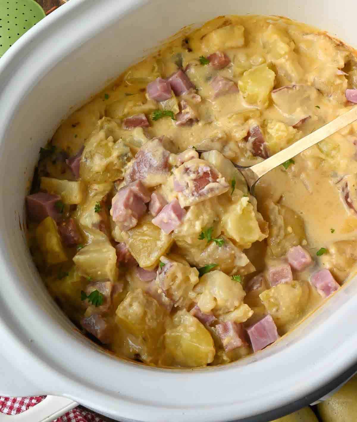 Ham and potatoes in a slow cooker scooped up with a serving spoon.