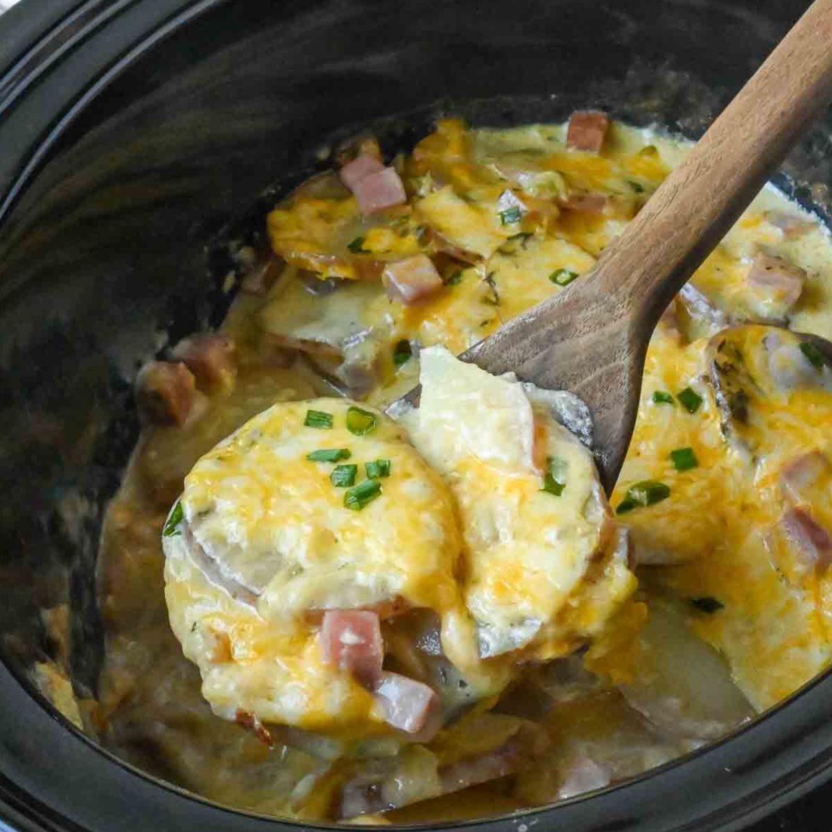 Ham and potatoes being scooped from a slow cooker.
