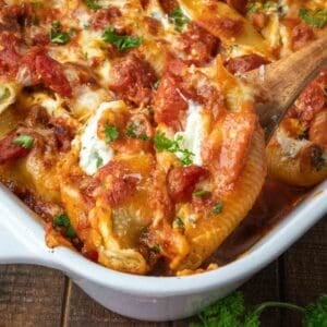 Taking a scoop of cheese stuffed shells from a baking dish with a wooden spoon.