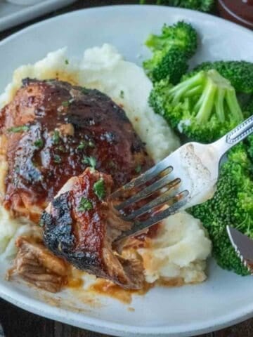 Bbq chicken thigh on a plate with mashed potatoes and broccoli.