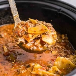 Taking a large scoop of lasagna soup out of a slow cooker with a ladle.