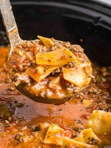 Taking a large scoop of lasagna soup out of a slow cooker with a ladle.