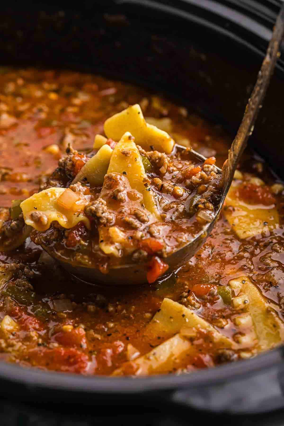 Ladling a large scoop of lasagna soup out of the crockpot.