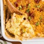 Close up of a wooden spoon taking a scoop of million dollar chicken casserole from a baking dish.