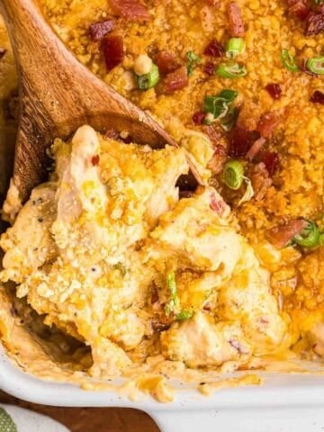 Close up of a wooden spoon taking a scoop of million dollar chicken casserole from a baking dish.