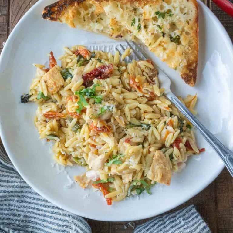 Tuscan chicken orzo on a plate with garlic bread.