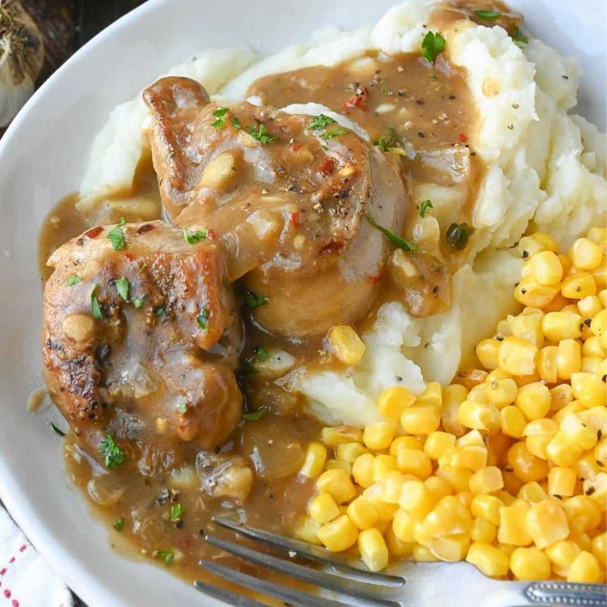 Plate of pork chops with mashed potatoes and corn niblets.