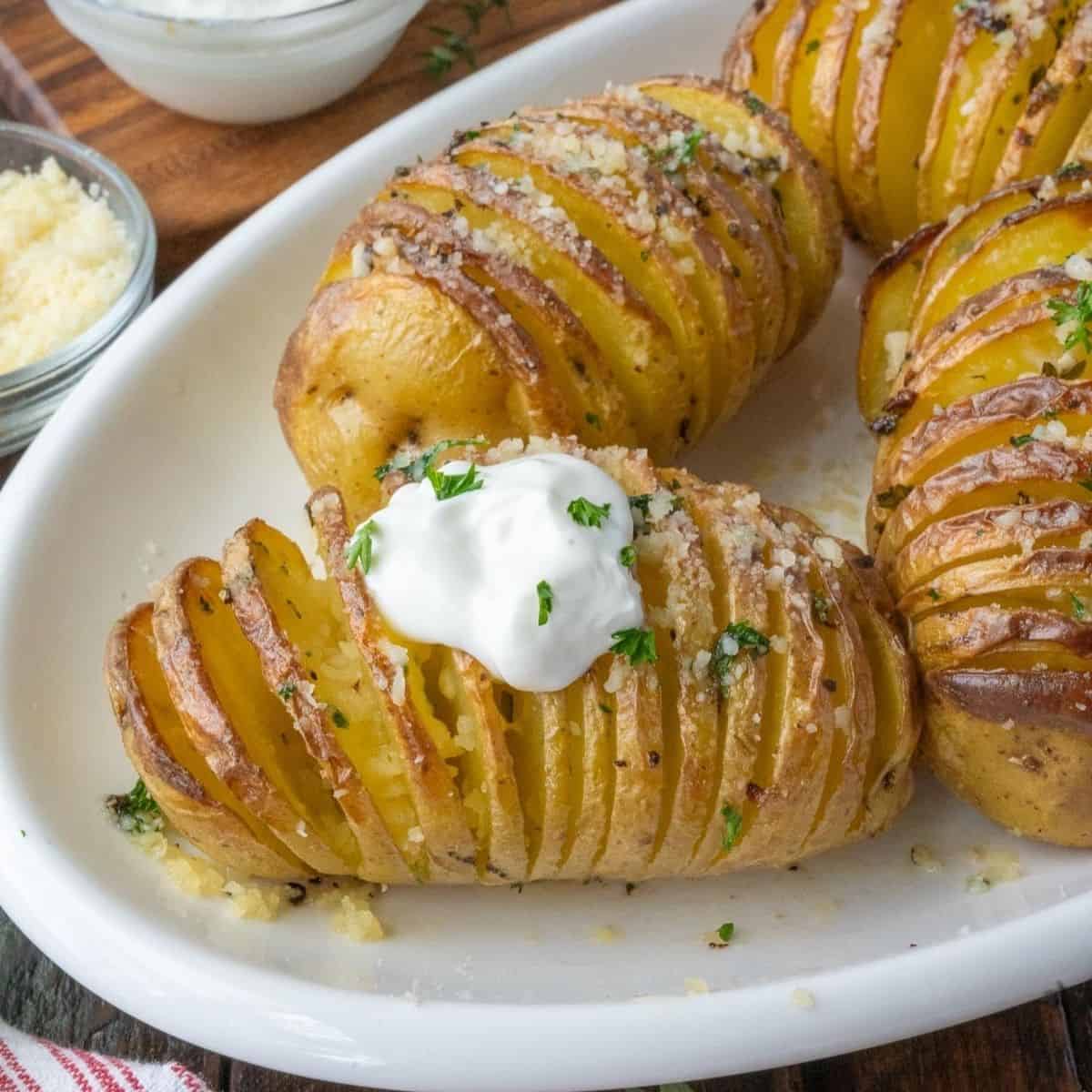 Side dish of hasselback potatoes topped with sour cream and chives.