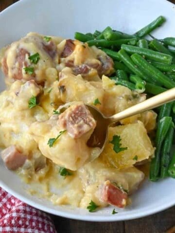 A spoon scooping up a bite of ham and potatoes.