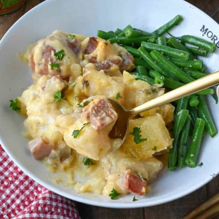 A spoon scooping up a bite of ham and potatoes.
