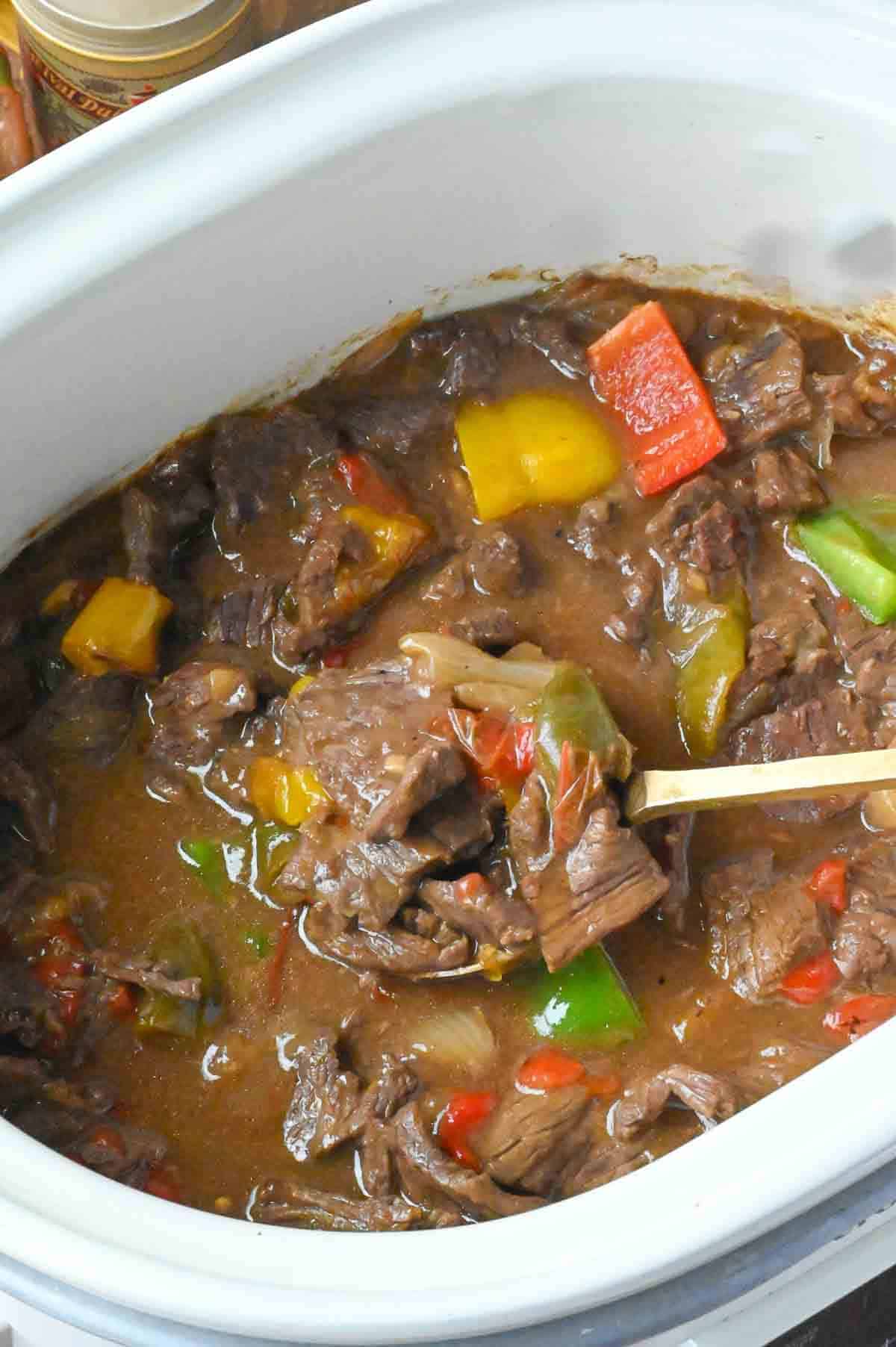 Stirring pepper steak in a slow cooker.