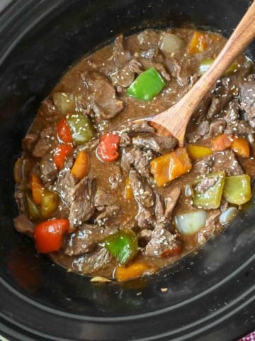 A serving spoon in a slow cooker with pepper steak.
