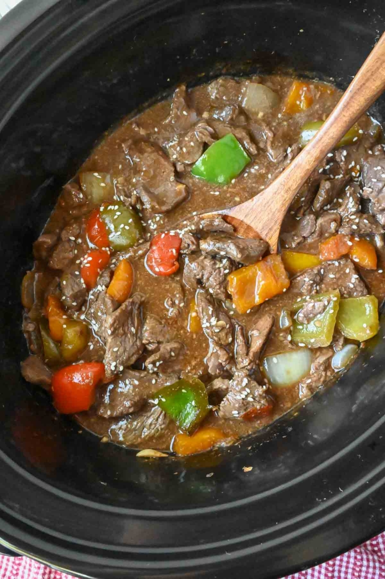 A serving spoon in a slow cooker with pepper steak.